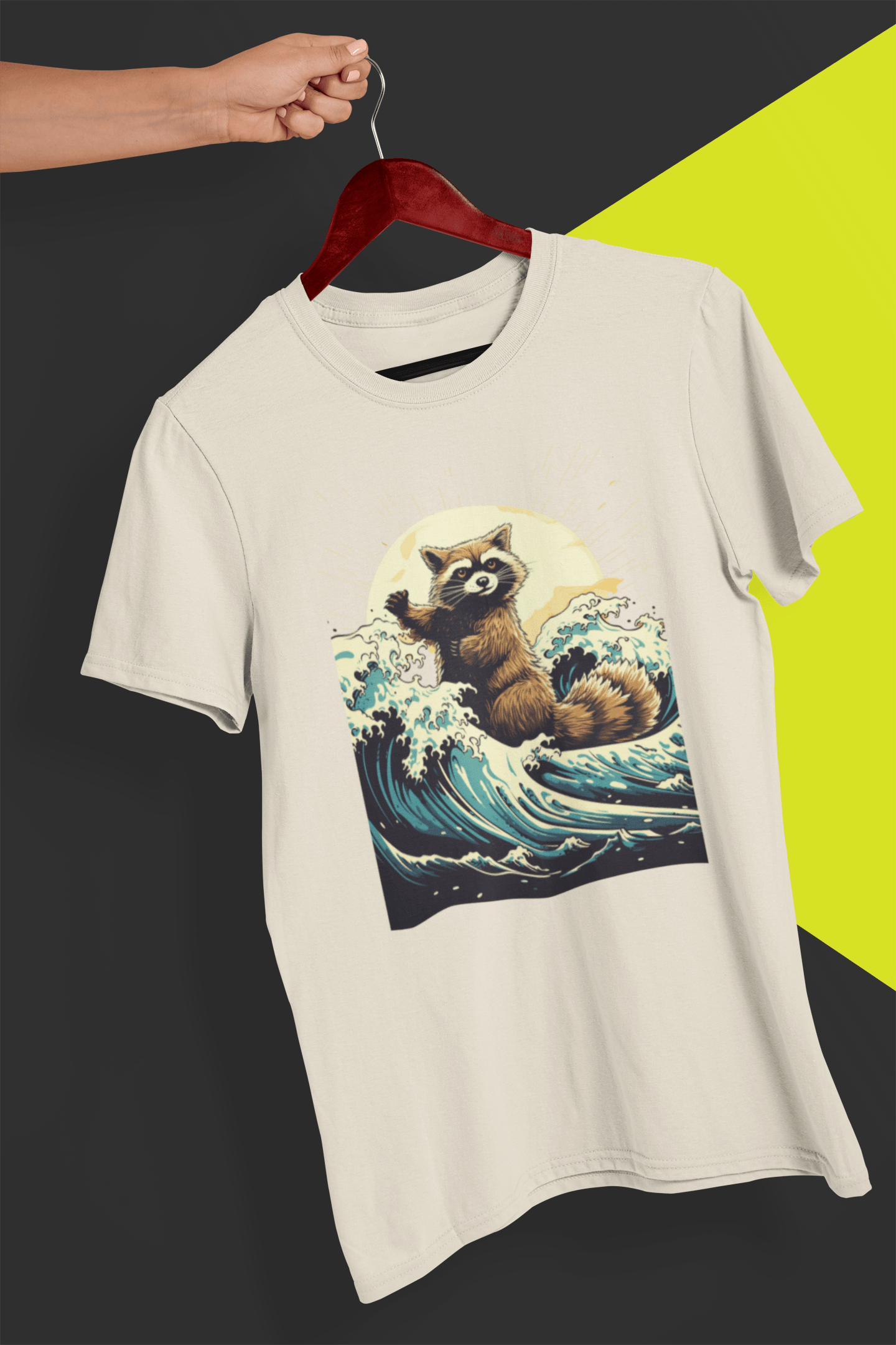 A sand T-shirt with an aesthetic racoon in the waves, is hung on a red hanger, held by a hand against a split black and yellow background.