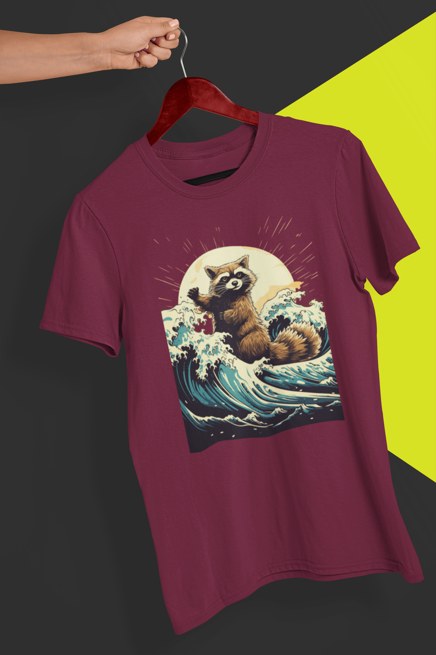 A dark red T-shirt with an aesthetic racoon in the waves, is hung on a red hanger, held by a hand against a split black and yellow background.