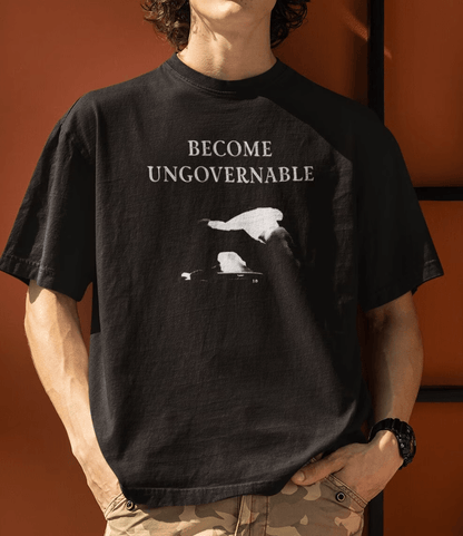 A man in front of an orange wall a black T-shirt with &quot;BECOME UNGOVERNABLE&quot; text and a white graphic of a leaping man onto a judge.