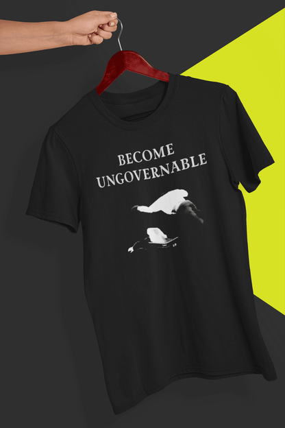 A black T-shirt with &quot;BECOME UNGOVERNABLE&quot; in black text and a white graphic of a leaping man onto a judge, held on a red hanger against a split black and yellow background.