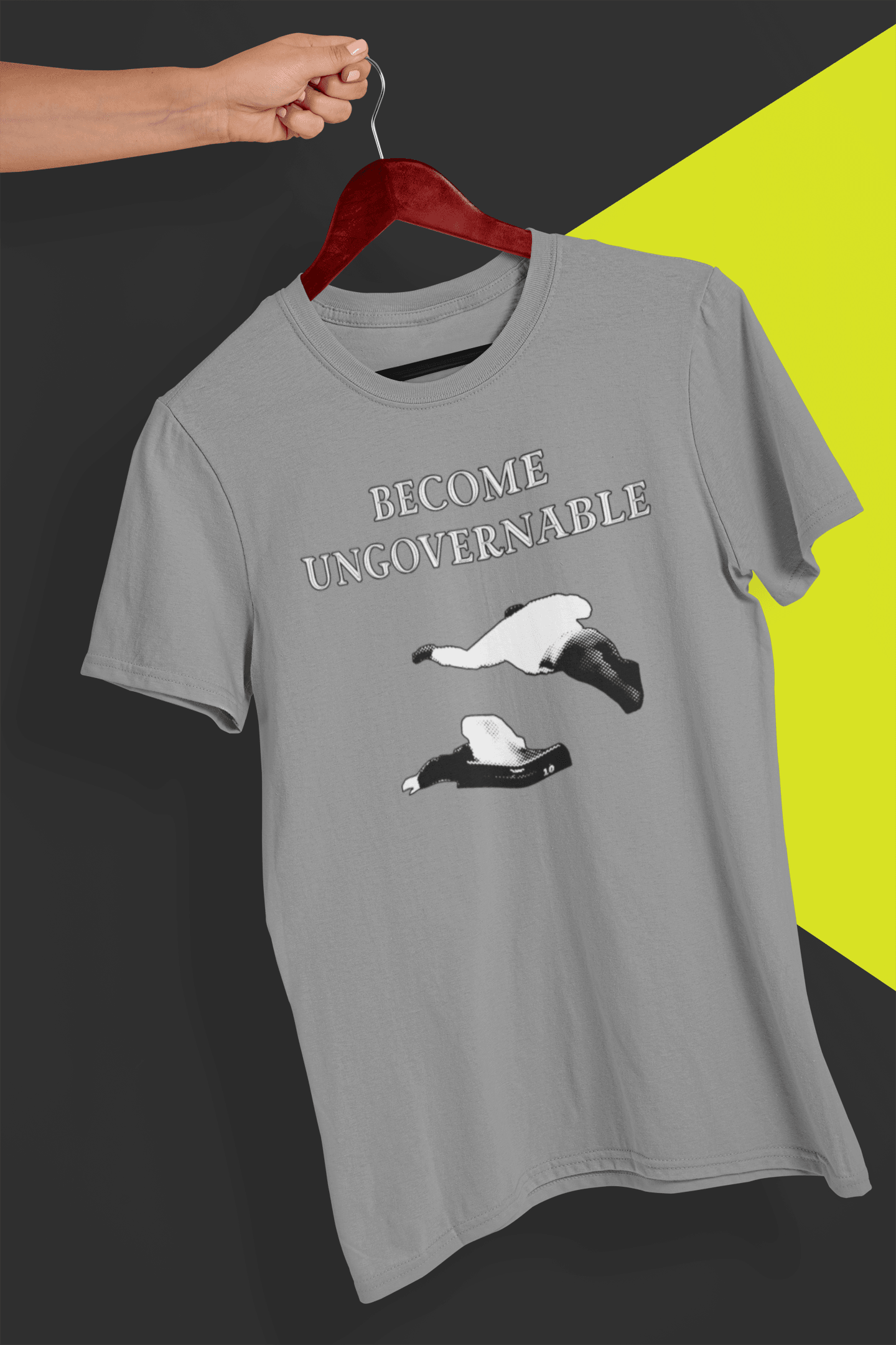 A gray T-shirt with &quot;BECOME UNGOVERNABLE&quot; in black text and a white graphic of a leaping man onto a judge, held on a red hanger against a split black and yellow background.