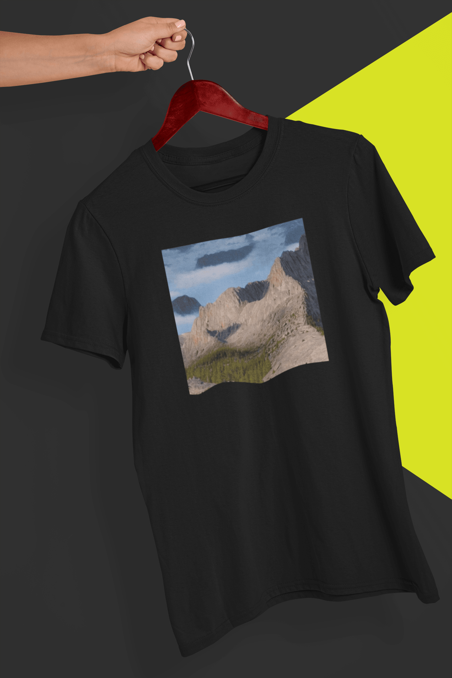 A black T-shirt featuring an AI generated landscape that looks like a cat taking a selfie staring at the camera, held by a hand against a split black and yellow background.