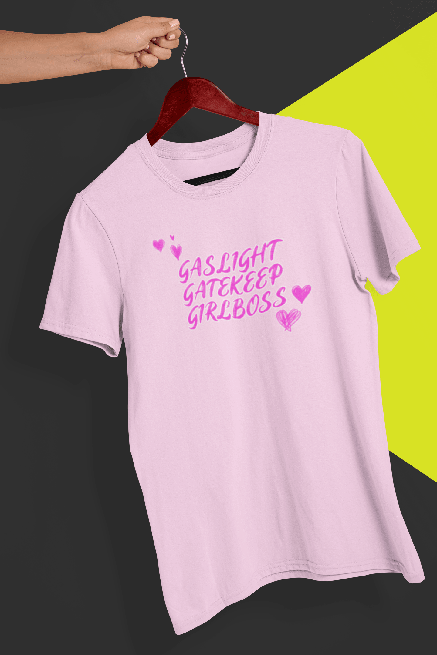 A pink T-shirt that says &quot;Gaslight, Gatekeep, Girlboss&quot;, held by a hand against a split black and yellow background.