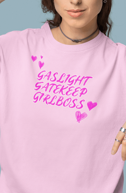 A woman wears a pink T-shirt that says &quot;Gaslight, Gatekeep, Girlboss&quot;.