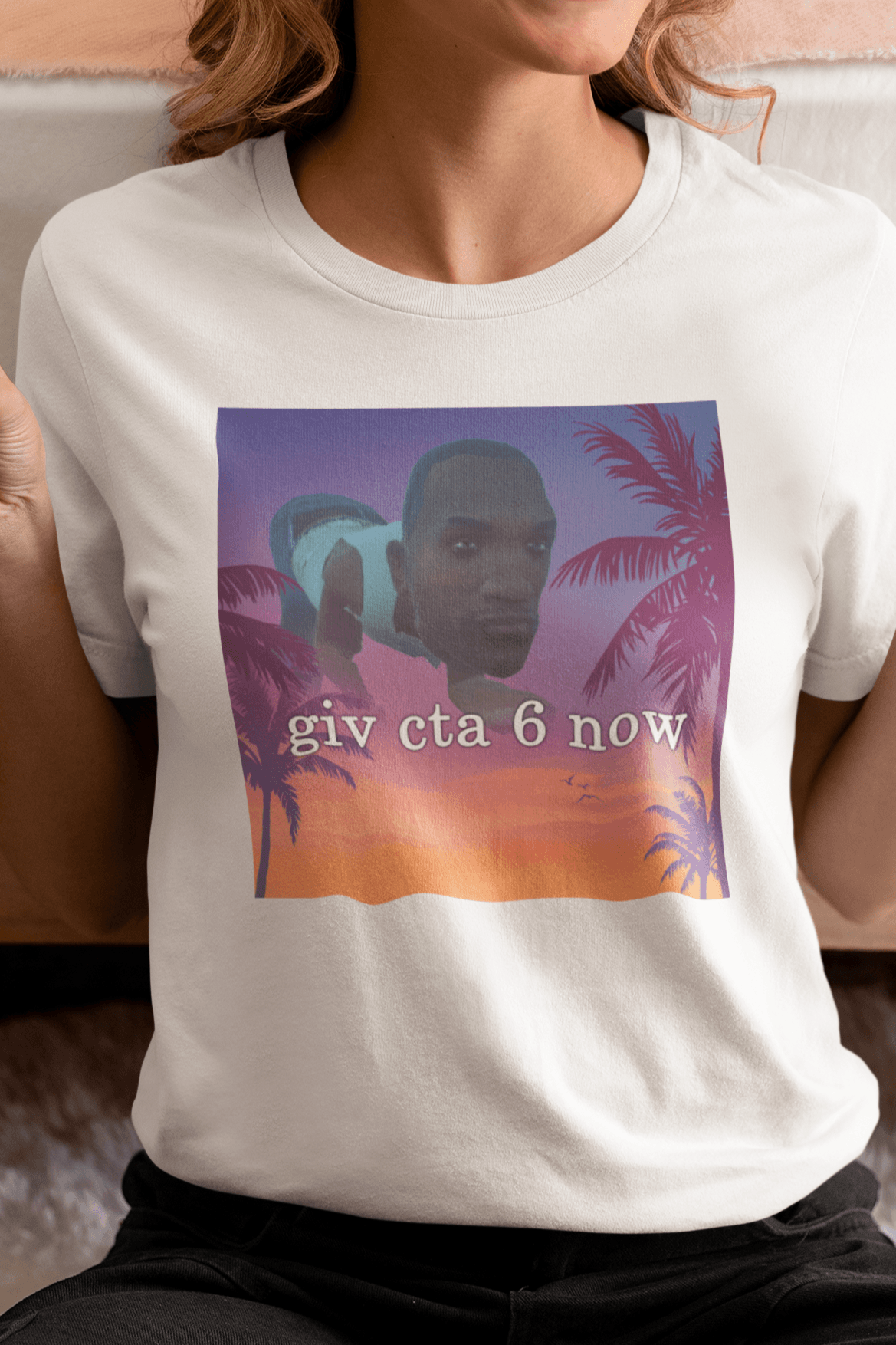 A woman wearing a white T-shirt with an aesthetic miami imagery and a funny depiction cj from GTA San Andreas in the background written &quot;giv cta 6 now&quot;