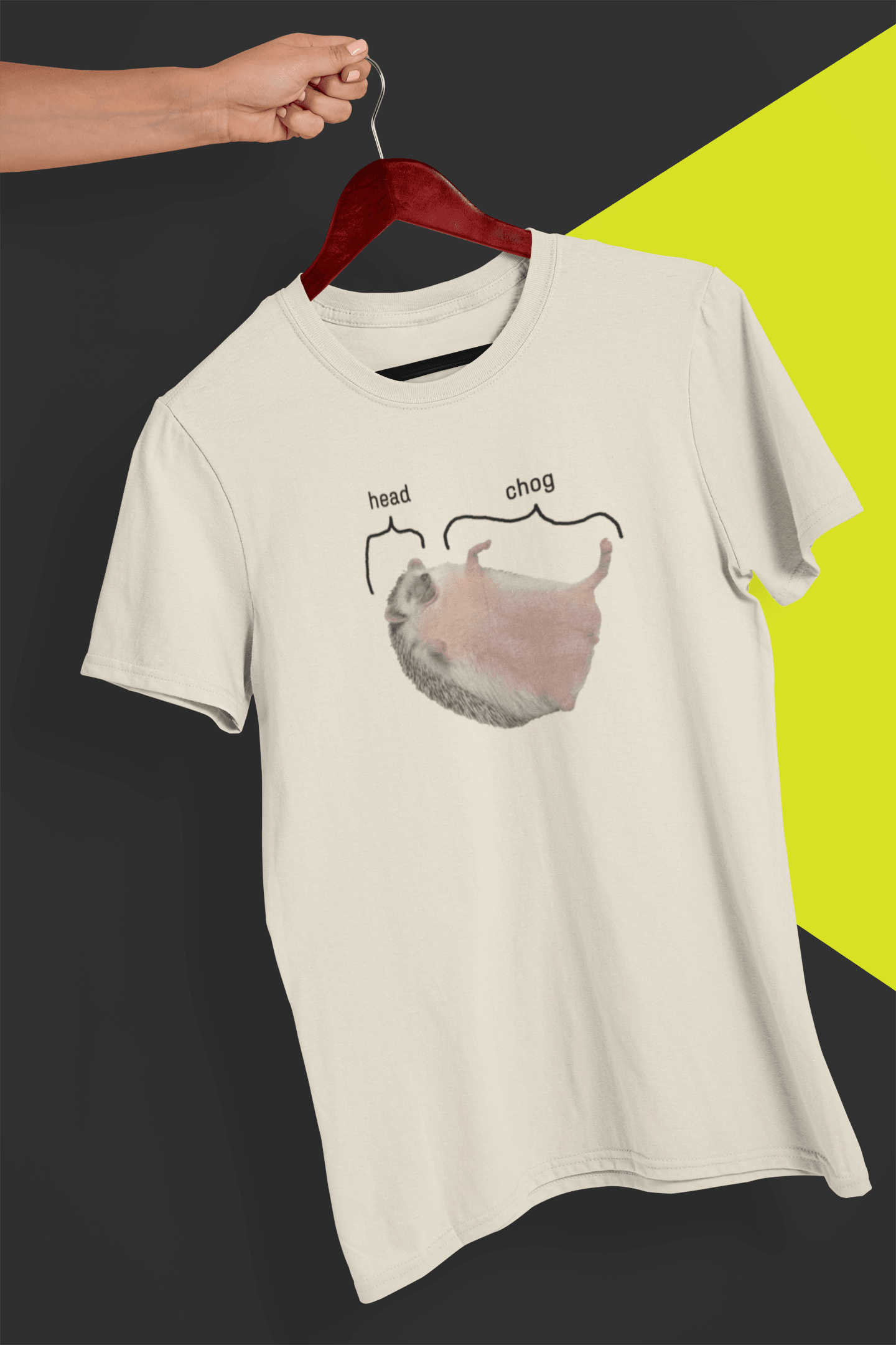 An off-white T-shirt featuring a cute hedgehog, which says &quot;head&quot; pointing at his head, and &quot;chog&quot; pointing at the rest of his body, is hung on a red hanger, held by a hand against a split black and yellow background.