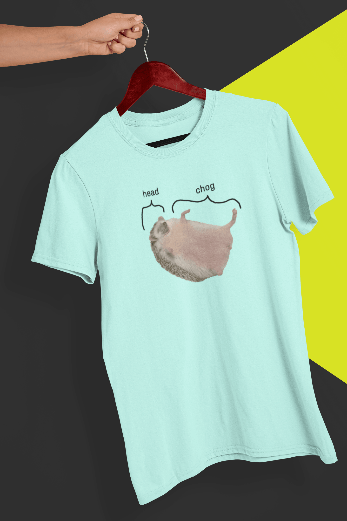 A baby-blue T-shirt featuring a cute hedgehog, which says &quot;head&quot; pointing at his head, and &quot;chog&quot; pointing at the rest of his body, is hung on a red hanger, held by a hand against a split black and yellow background.