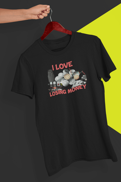 A black T-shirt with a graphs and cryptos written &quot;I Live Losing Money&quot;, held by a hand against a split black and yellow background.