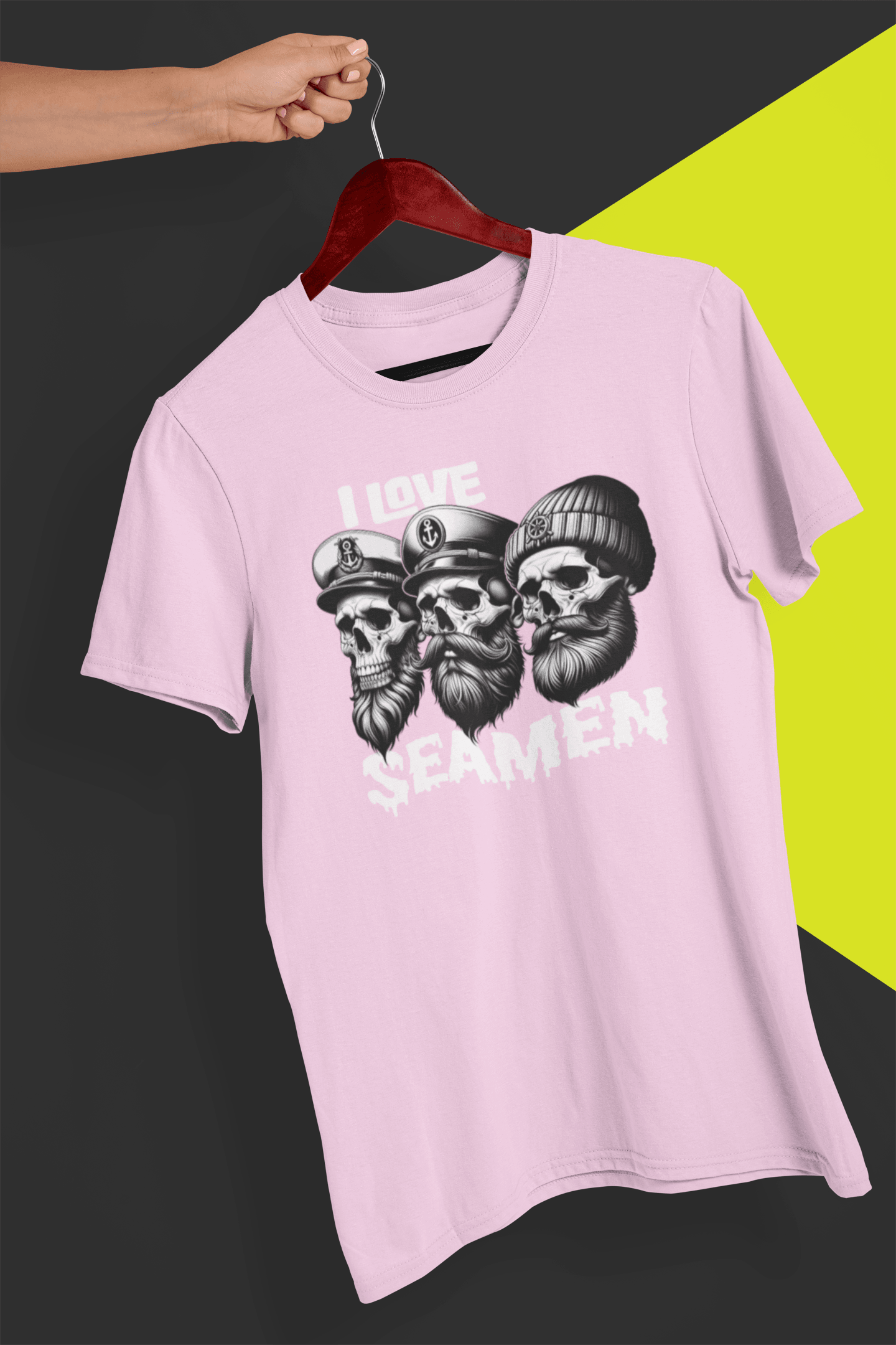 A light-pink T-shirt with three men of the sea written &quot;I Love Seamen&quot;. is hung on a red hanger, held by a hand against a split black and yellow background.