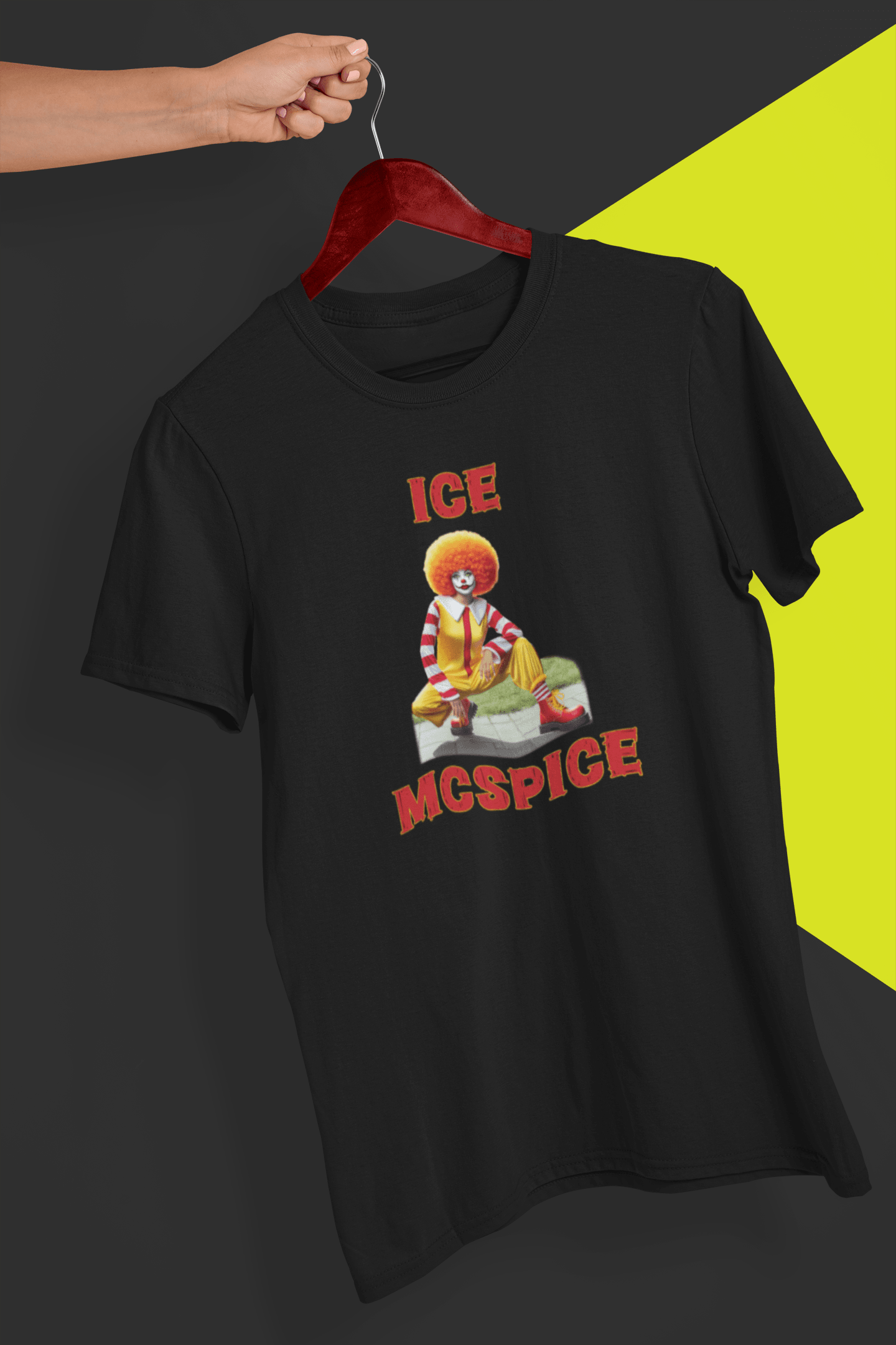 A black T-shirt featuring a woman who looks like the rapper Ice Spice dressed as Ronald McDonald, saying &quot;Ice McSpice&quot;, held by a hand against a split black and yellow background.