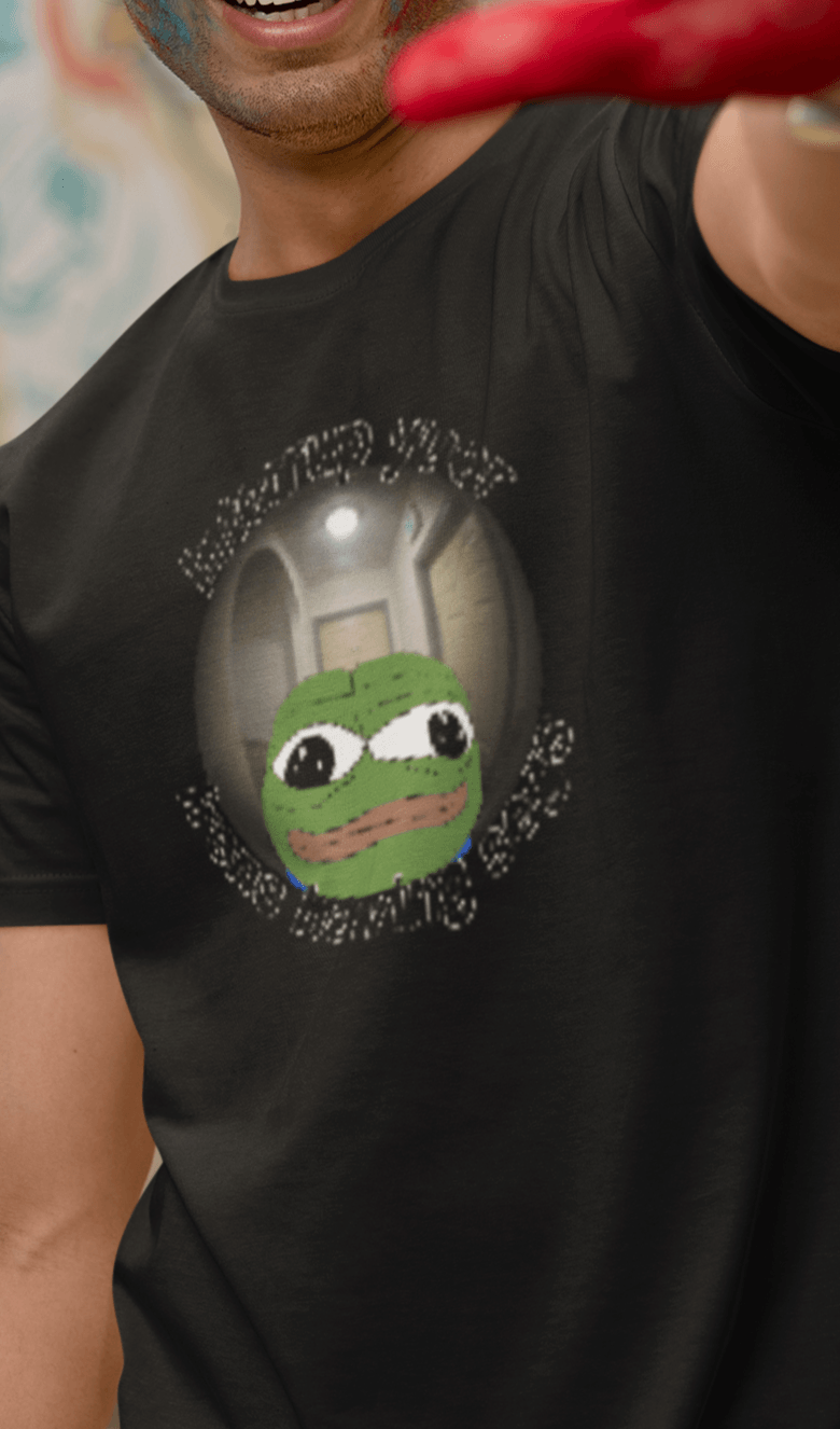 A man wears a black T-shirt featuring a peepo frog on the other side of a door peephole, saying &quot;Interrupt your friends having sex&quot; full of typos