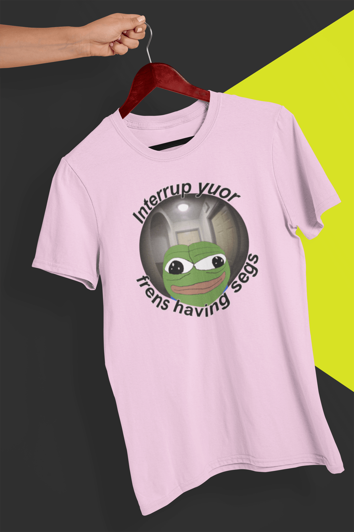 A pink T-shirt featuring a peepo frog on the other side of a door peephole, saying &quot;Interrupt your friends having sex&quot; full of typos, held by a hand against a split black and yellow background.