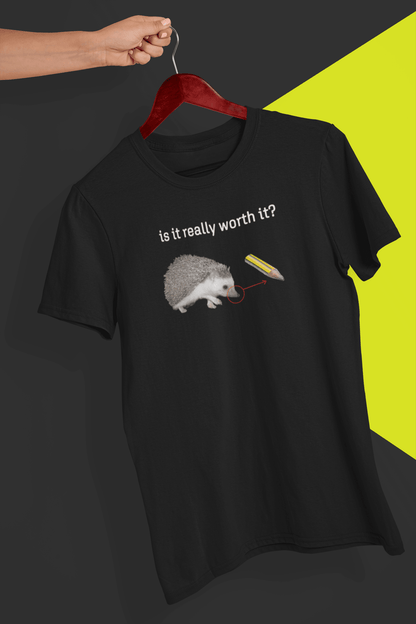 A black T-shirt with a cute hedgehog, showing the similarity between its nose and the tip of a pencil, saying &quot;is it really worth it?&quot;, is hung on a red hanger, held by a hand against a split black and yellow background.