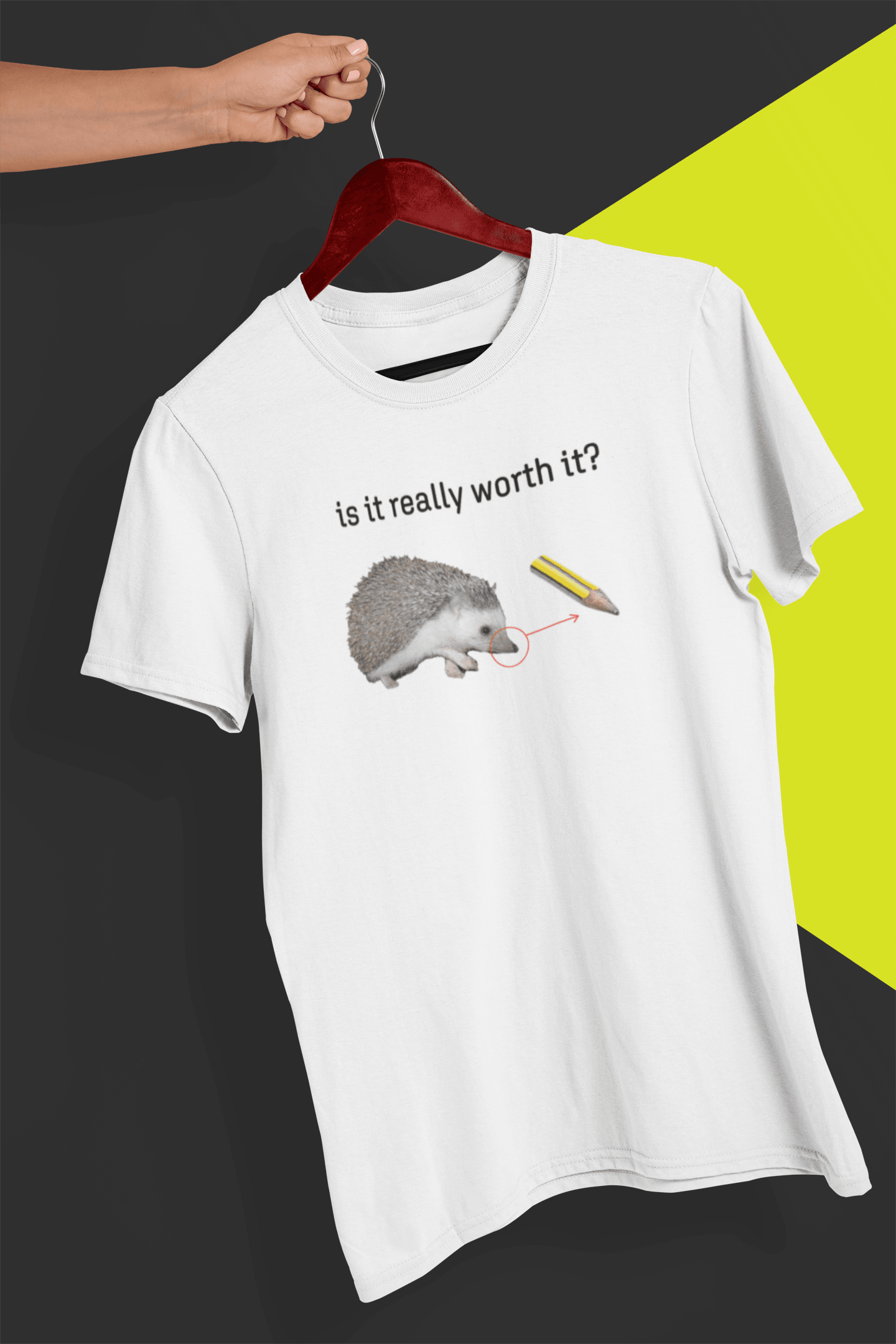 A white T-shirt with a cute hedgehog, showing the similarity between its nose and the tip of a pencil, saying &quot;is it really worth it?&quot;, is hung on a red hanger, held by a hand against a split black and yellow background.