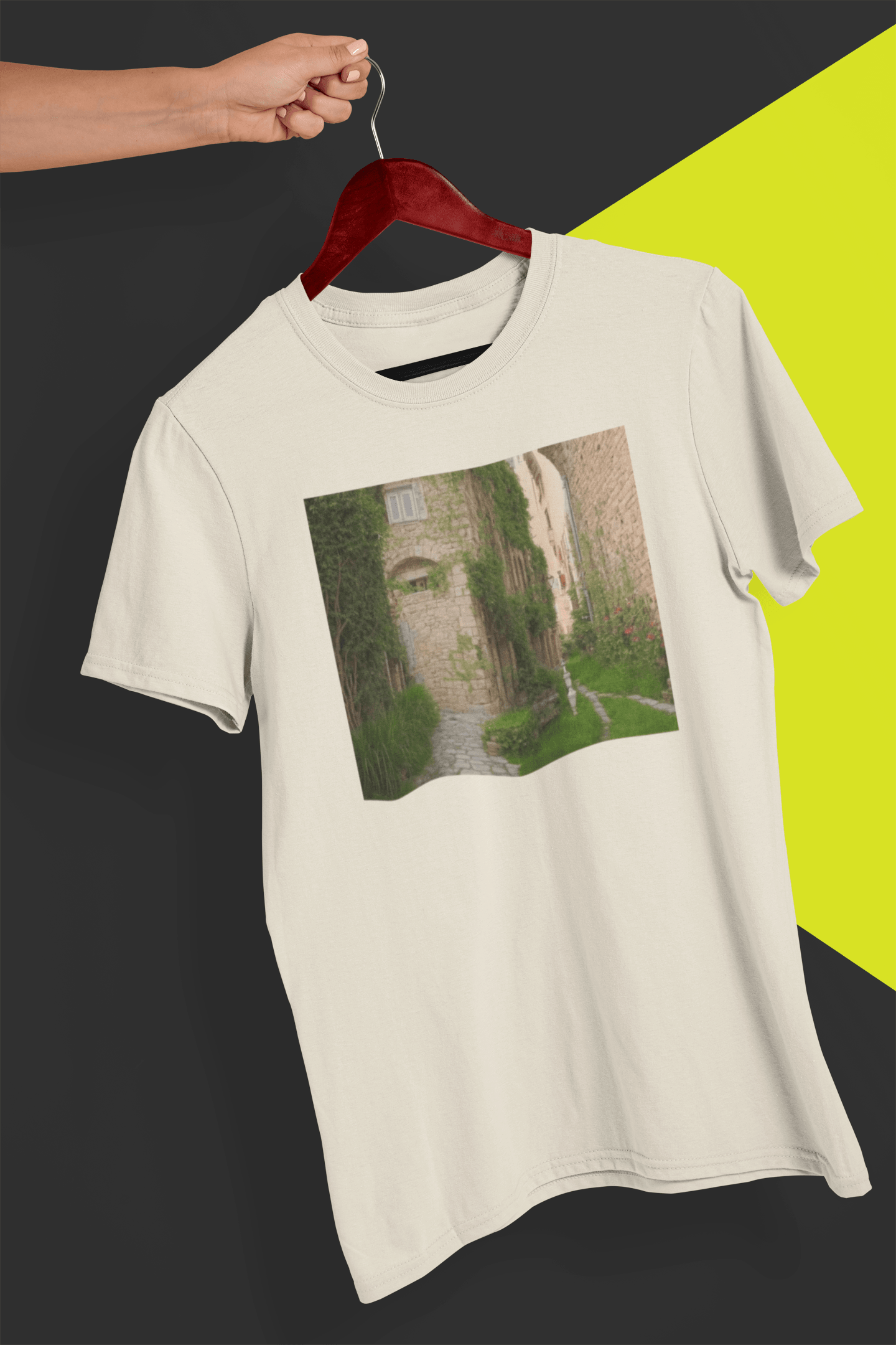 An off-white T-shirt featuring a landscape generated by artificial intelligence that looks like Jimmy or Saul from Better Call Saul and Breaking Bad, is hung on a red hanger, held by a hand against a split black and yellow background.