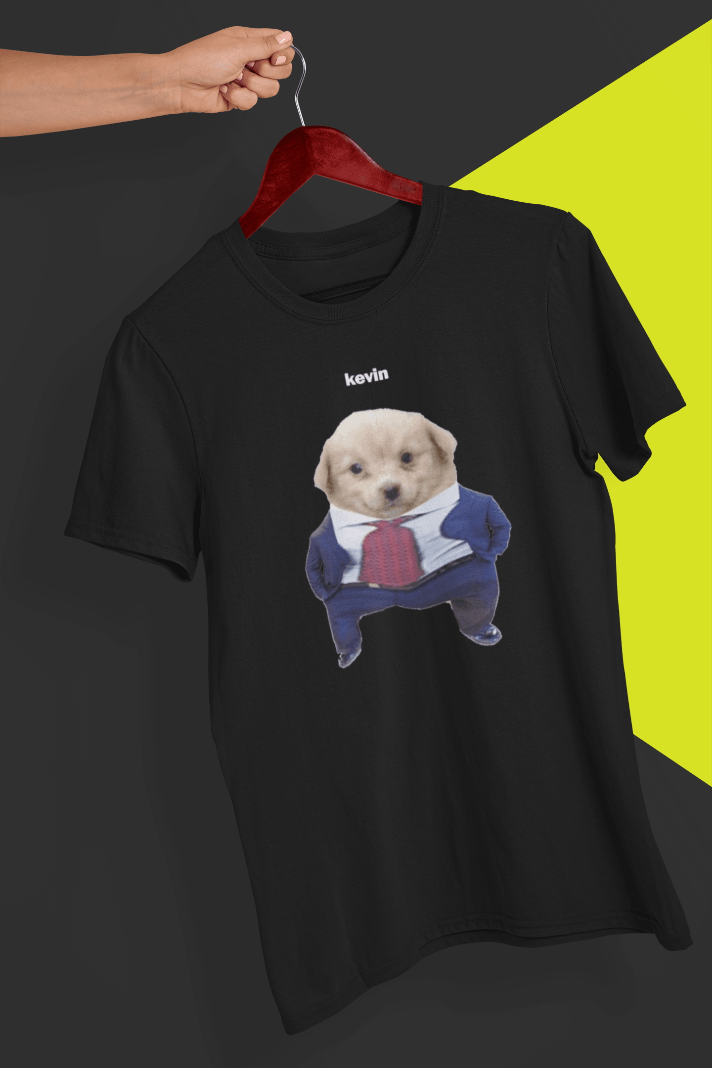 A black T-shirt with a cute dog wearing a suit written &quot;kevin&quot; on top of him, is hung on a red hanger, held by a hand against a split black and yellow background.