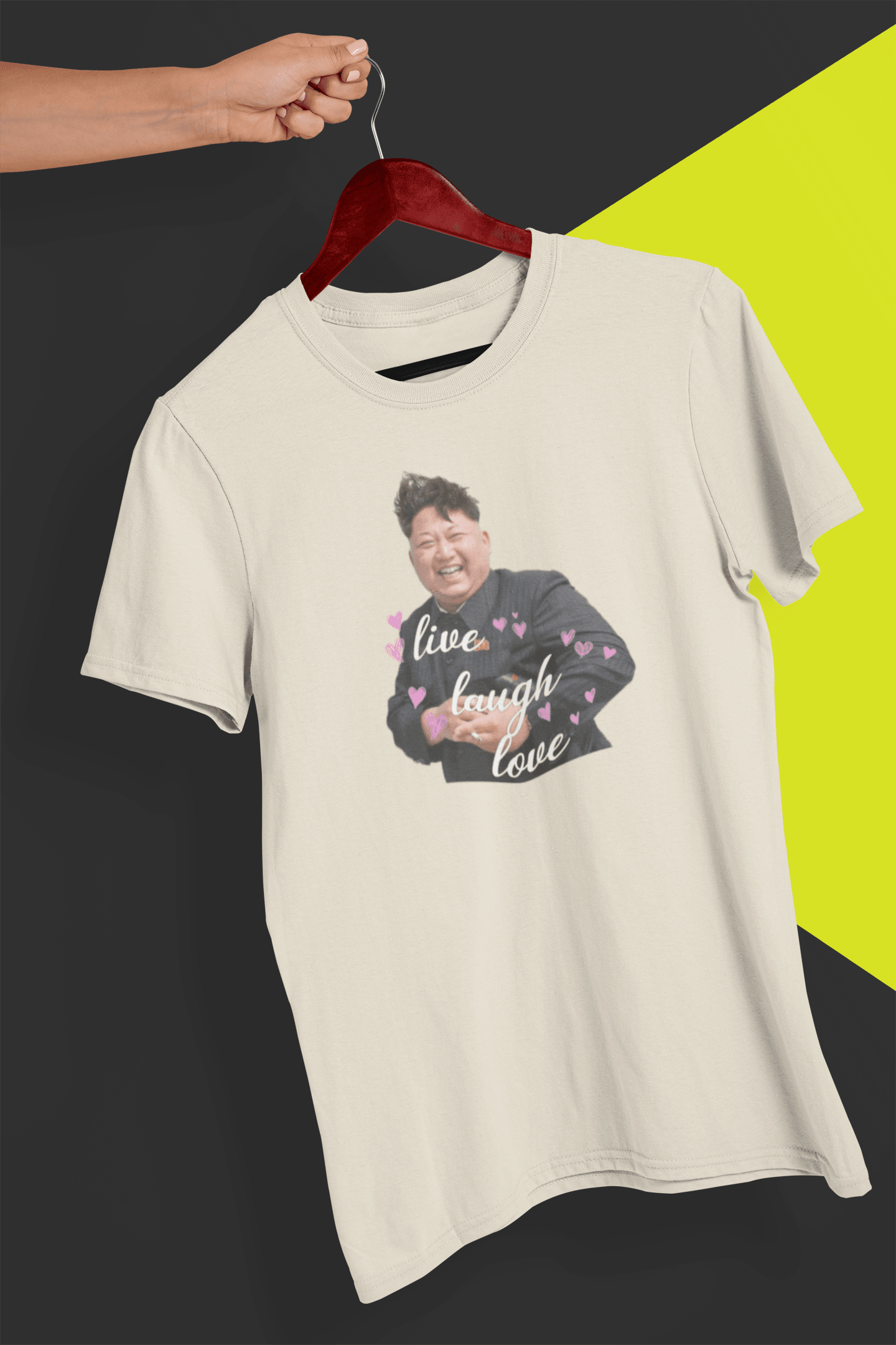 A off-white T-shirt of kim jong un laughing saying &quot;Live Laugh Love&quot;, held by a hand against a split black and yellow background.