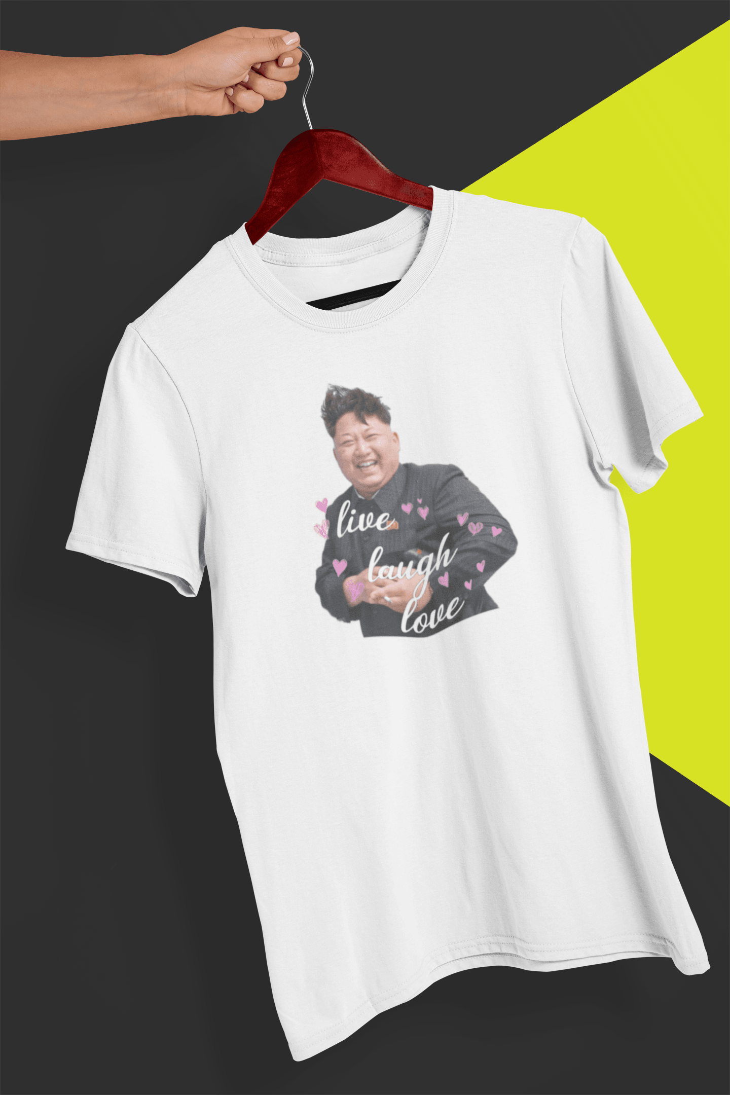 A white T-shirt of kim jong un laughing saying &quot;Live Laugh Love&quot;, held by a hand against a split black and yellow background.