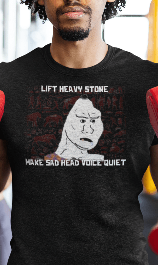 A man wears a black T-shirt featuring a neanderthal looking drawing, saying &quot;lift heavy stone make sad head voice quiet&quot;.