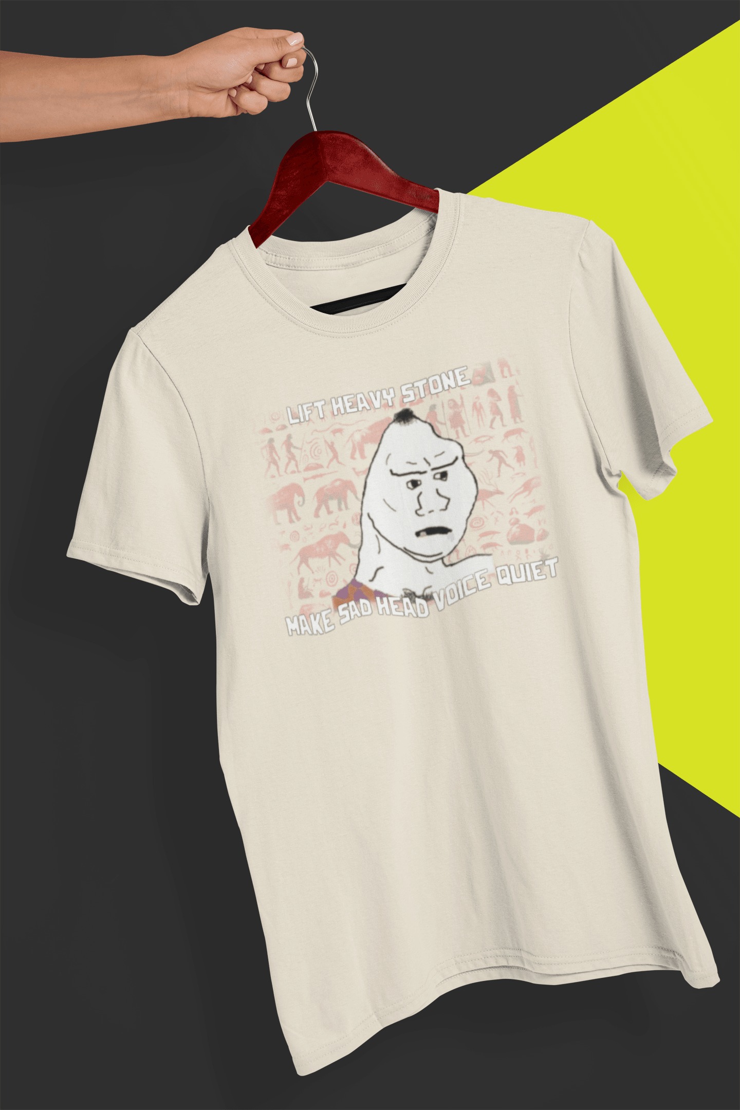 An off-white T-shirt with a neanderthal looking drawing, saying &quot;lift heavy stone make sad head voice quiet&quot;, held by a hand against a split black and yellow background.