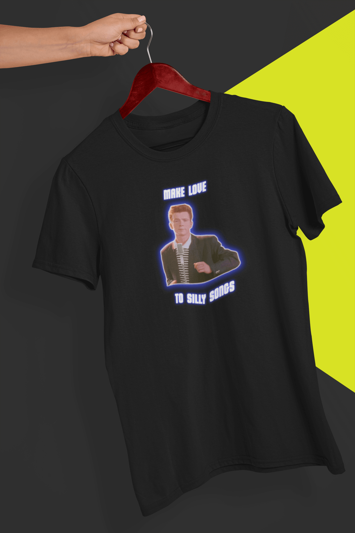 A black T-shirt with a depiction of Rick Astley that says &quot;Make Love To Silly Songs&quot;, held by a hand against a split black and yellow background.