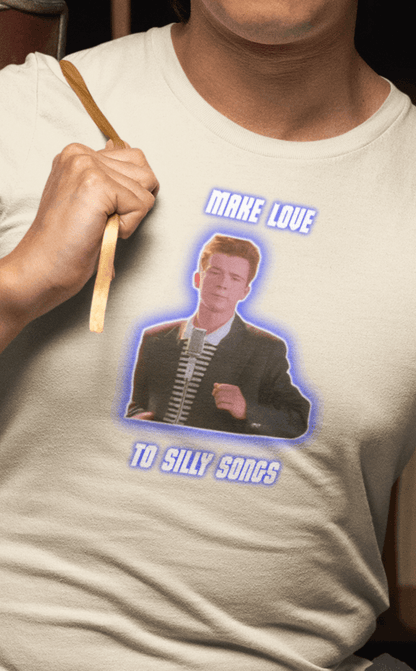 A man wears an off-white T-shirt with a depiction of Rick Astley that says &quot;Make Love To Silly Songs&quot;.