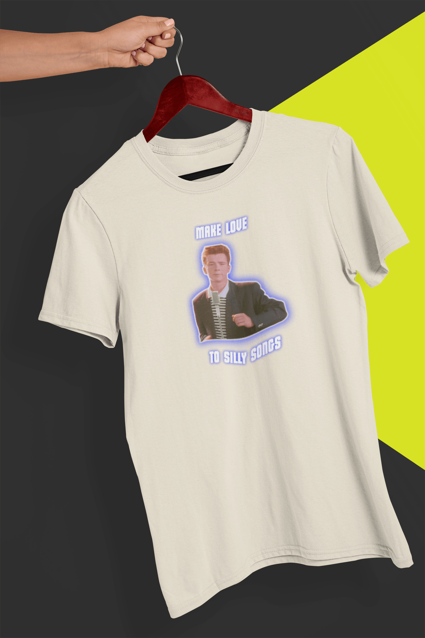 An off-white T-shirt with a depiction of Rick Astley that says &quot;Make Love To Silly Songs&quot;, held by a hand against a split black and yellow background.