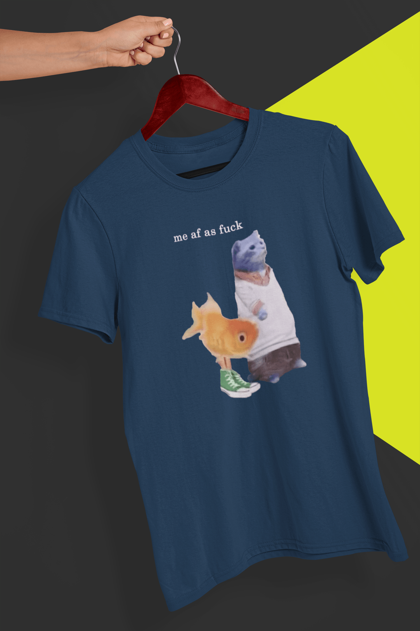 A navy blue T-shirt with a cute cat and fish portraying Gumball and Darwin with &quot;me af as fuck&quot; written on top, is hung on a red hanger, held by a hand against a split black and yellow background.