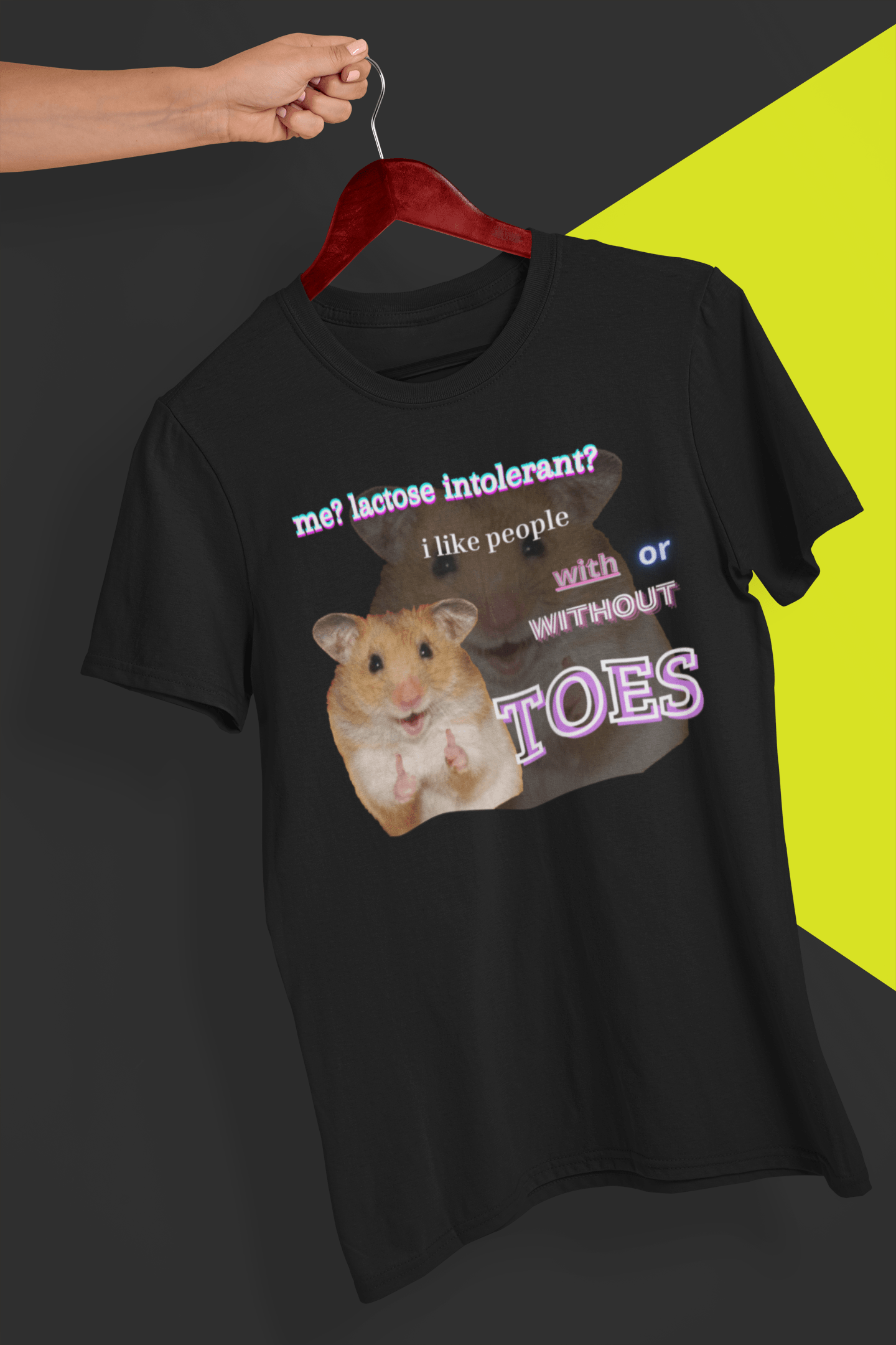 A black T-shirt with a a cute hamster doin a thumbs up written &quot;Me? Lactose intolerant? I like people with or without TOES&quot;, is hung on a red hanger, held by a hand against a split black and yellow background.