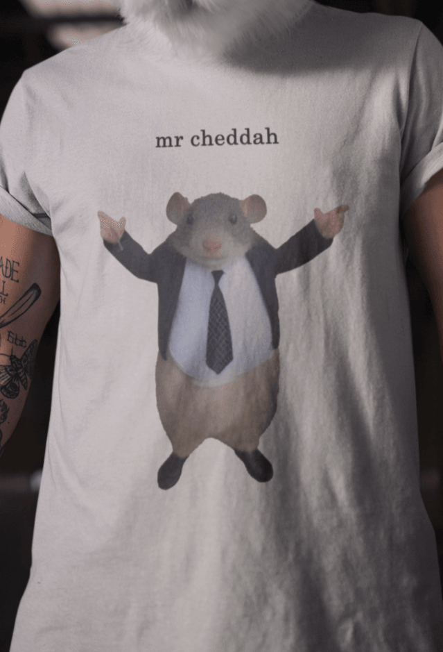 A man wears a white T-shirt featuring a cute rat wearing a suit written &quot;mr cheddah&quot; on top of him.