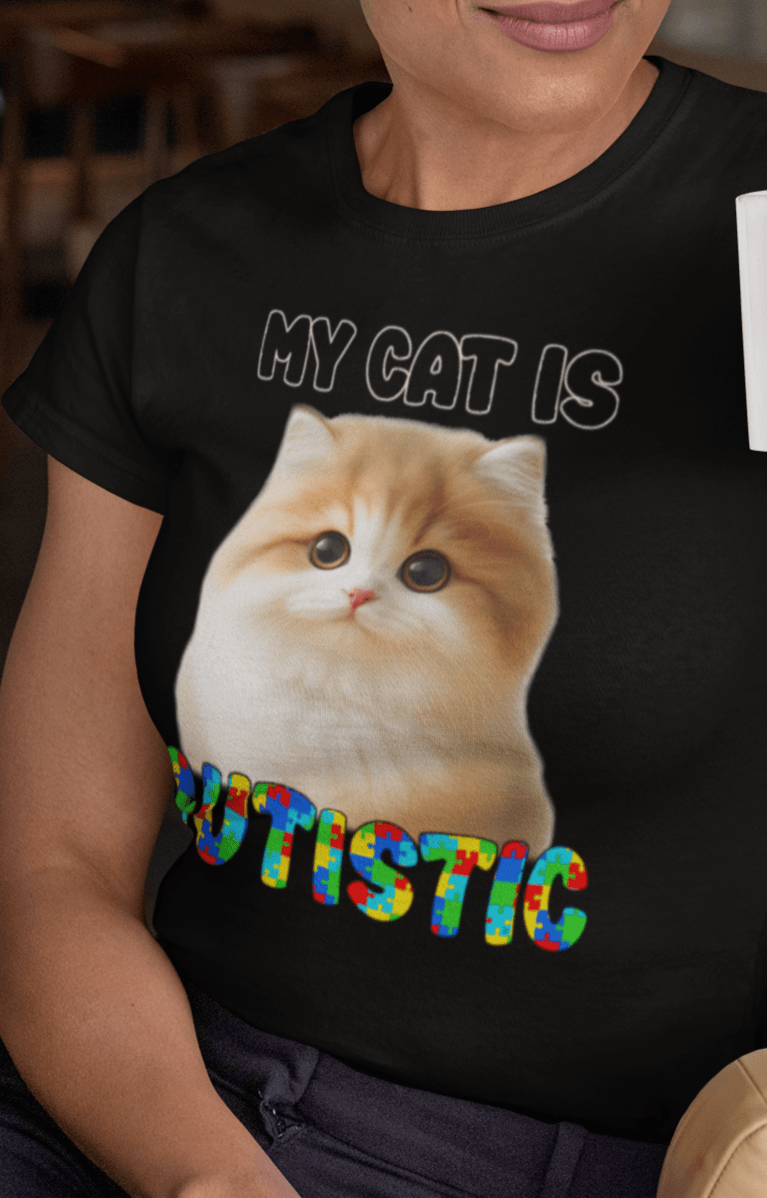 A woman wears an black T-shirt featuring a cute cat written &quot;My Cat is Autistic&quot; on top.