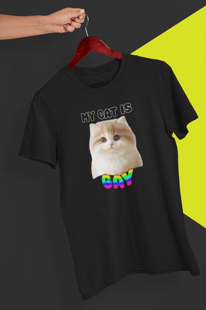 A black T-shirt with a cute cat written &quot;My Cat is Gay&quot; on top, is hung on a red hanger, held by a hand against a split black and yellow background.