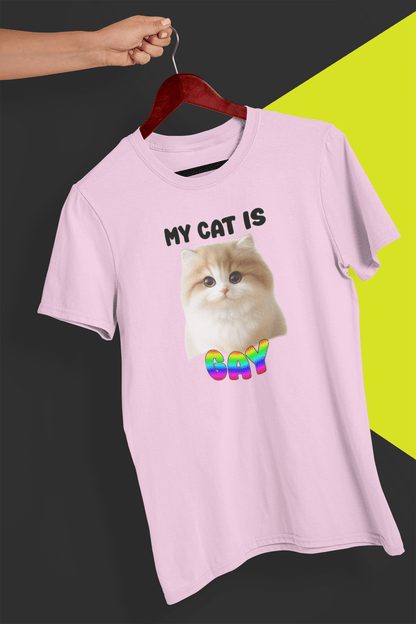 A pink T-shirt with a cute cat written &quot;My Cat is Gay&quot; on top, is hung on a red hanger, held by a hand against a split black and yellow background.