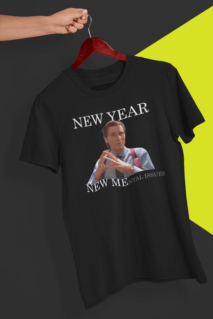 A black T-shirt with Christian Bale in american psycho, saying &quot;New Year, New Mental Issues&quot;, held by a hand against a split black and yellow background.