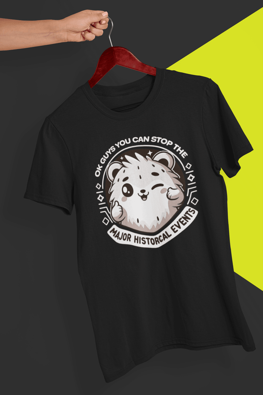 A black T-shirt with a cute hamster doing a thumbs up written &quot;OK GUYS YOU CAN STOP THE MAJOR HISTORICAL EVENTS&quot;. is hung on a red hanger, held by a hand against a split black and yellow background.