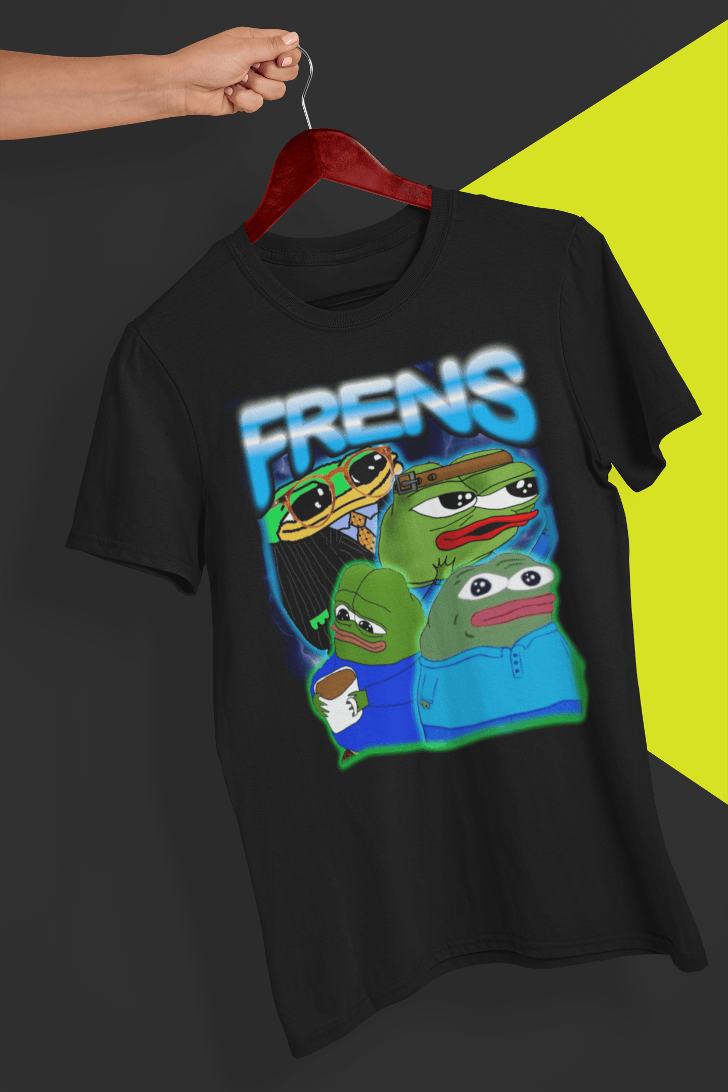 A black T-shirt with four cute pepes and peepos written &quot;FRENS&quot; on top, is hung on a red hanger, held by a hand against a split black and yellow background.