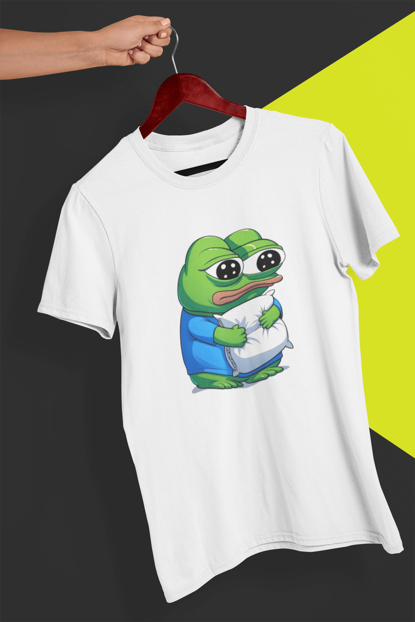 A white T-shirt with a cute apu apustaja pepe in the middle hugging a pillow, held by a hand against a split black and yellow background.