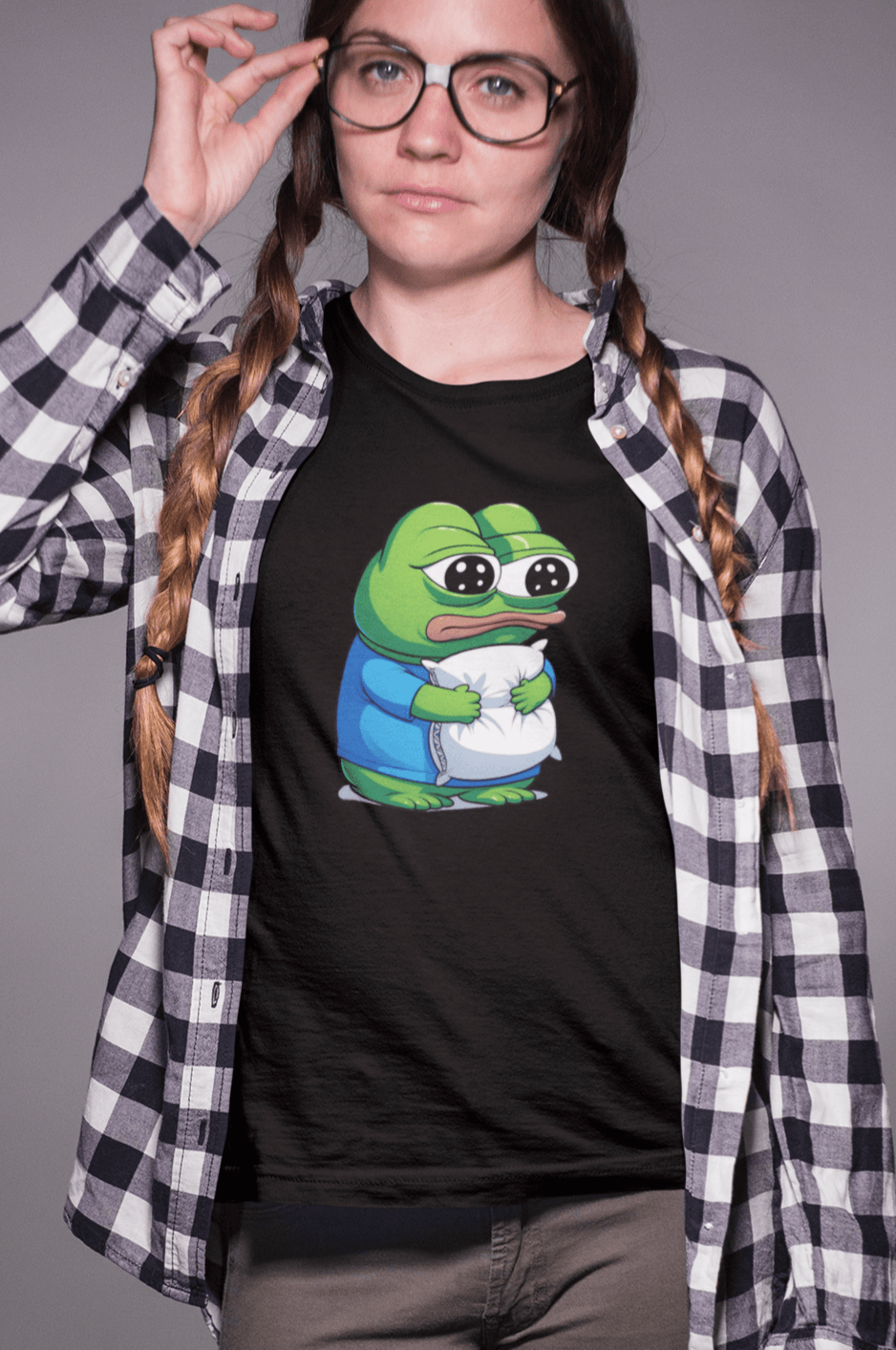 A woman wears a black T-shirt featuring a cute apu apustaja pepe in the middle hugging a pillow.