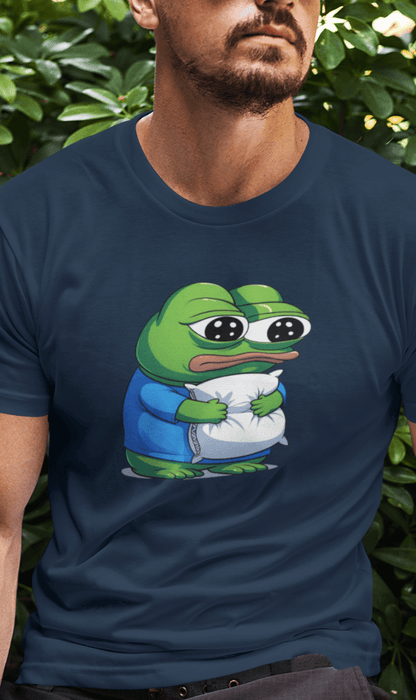 A man wears a navy-blue T-shirt featuring a cute apu apustaja pepe in the middle hugging a pillow.