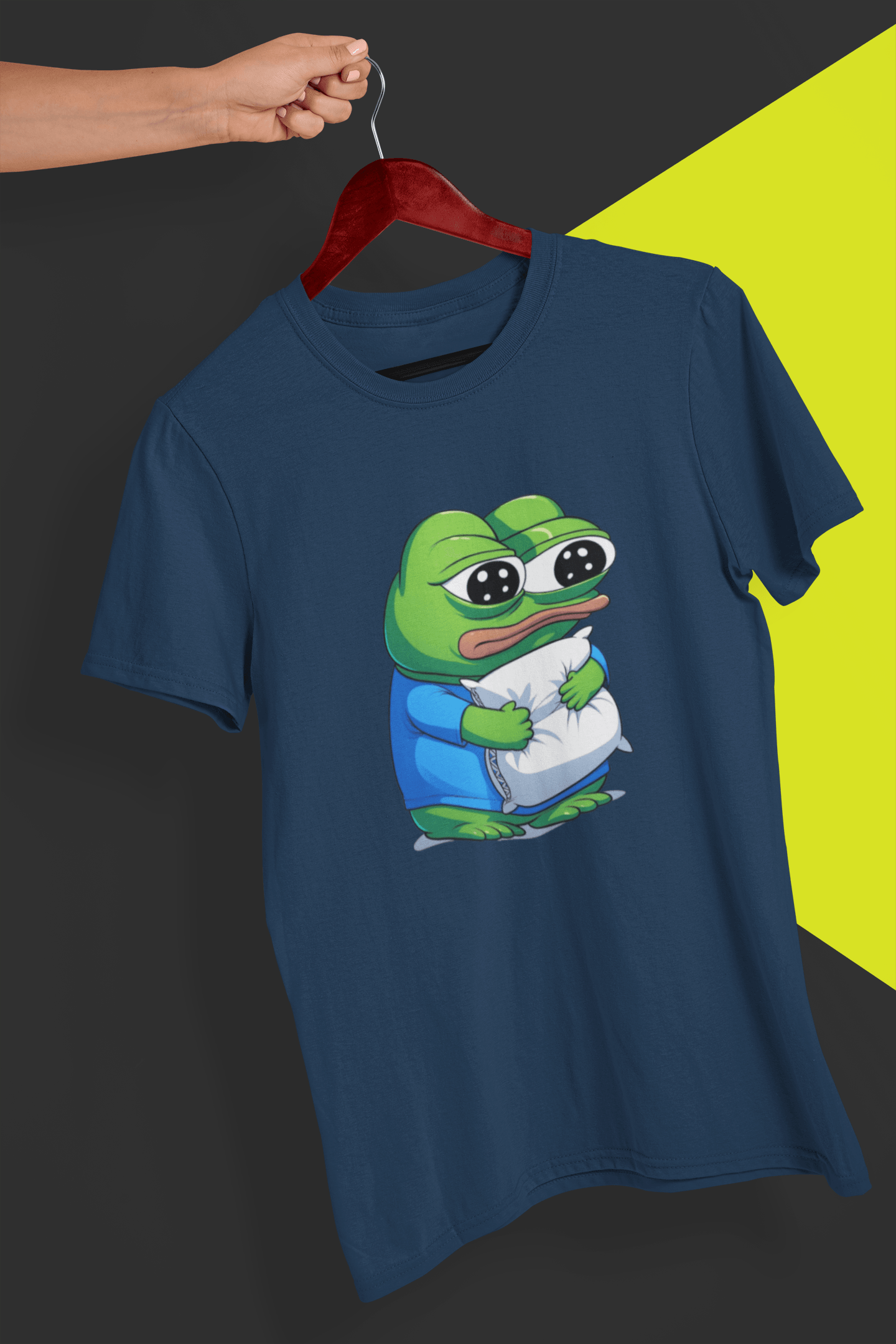 A navy blue T-shirt with a cute apu apustaja pepe in the middle hugging a pillow, held by a hand against a split black and yellow background.