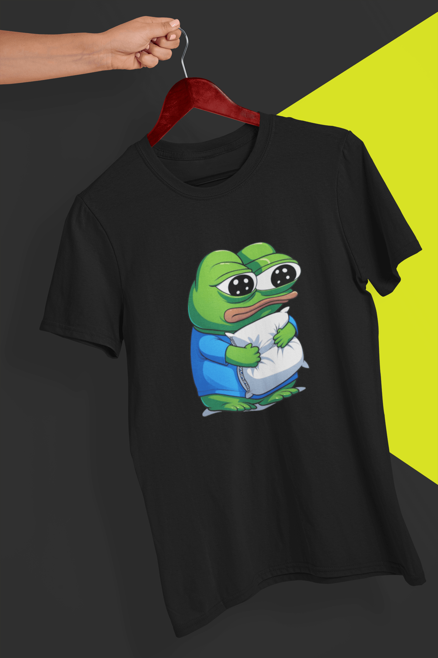 A black T-shirt with a cute apu apustaja pepe in the middle hugging a pillow, held by a hand against a split black and yellow background.