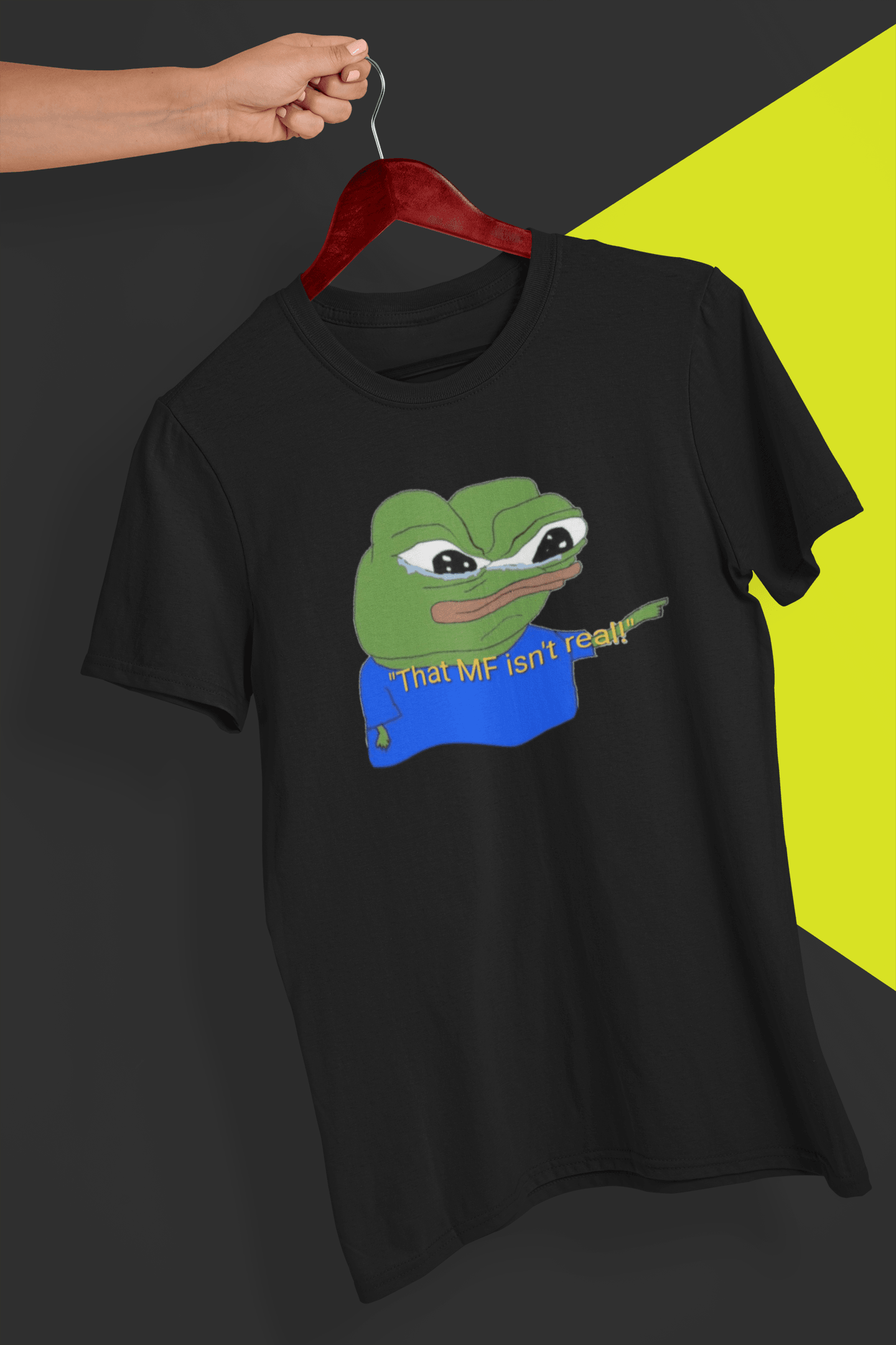 A black T-shirt with a cute apu apustaja pepe in the middle pointing and written &quot;That MF isn&#39;t real!&quot;, held by a hand against a split black and yellow background.