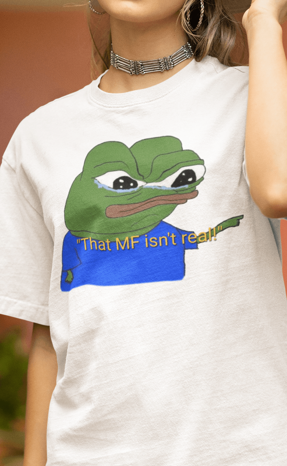 A woman wears a white T-shirt featuring a cute apu apustaja pepe in the middle pointing and written &quot;That MF isn&#39;t real!&quot;.