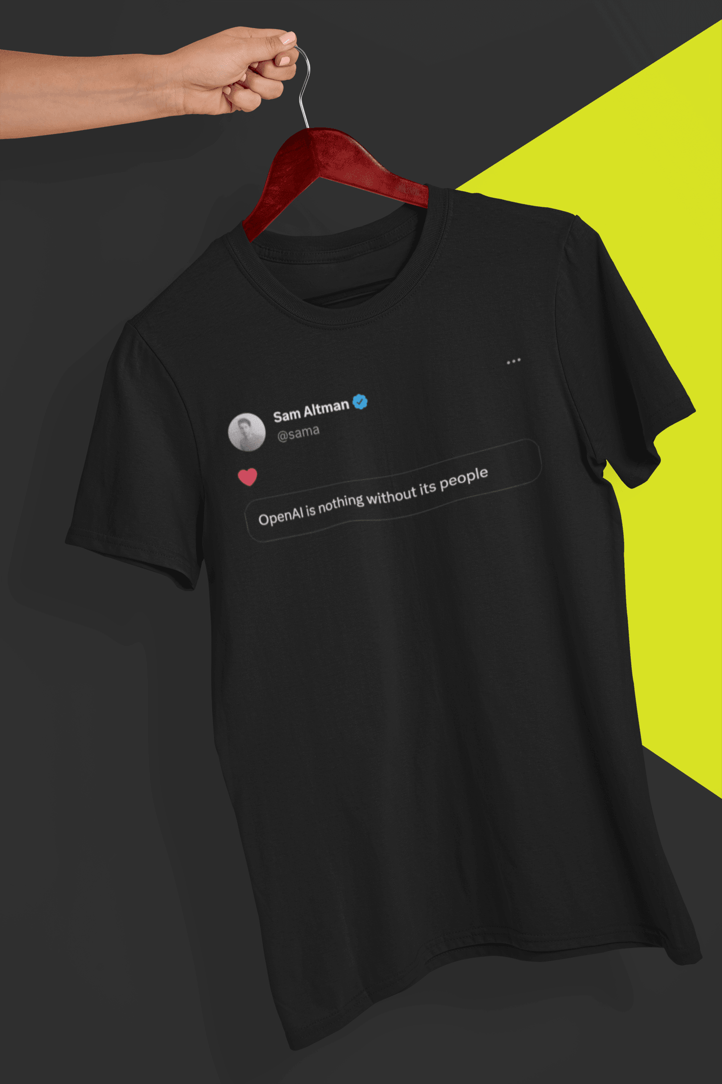 A black T-shirt with a tweet from Sam Altman that says &quot;OpenAI is nothing without its people&quot;, is hung on a red hanger, held by a hand against a split black and yellow background.