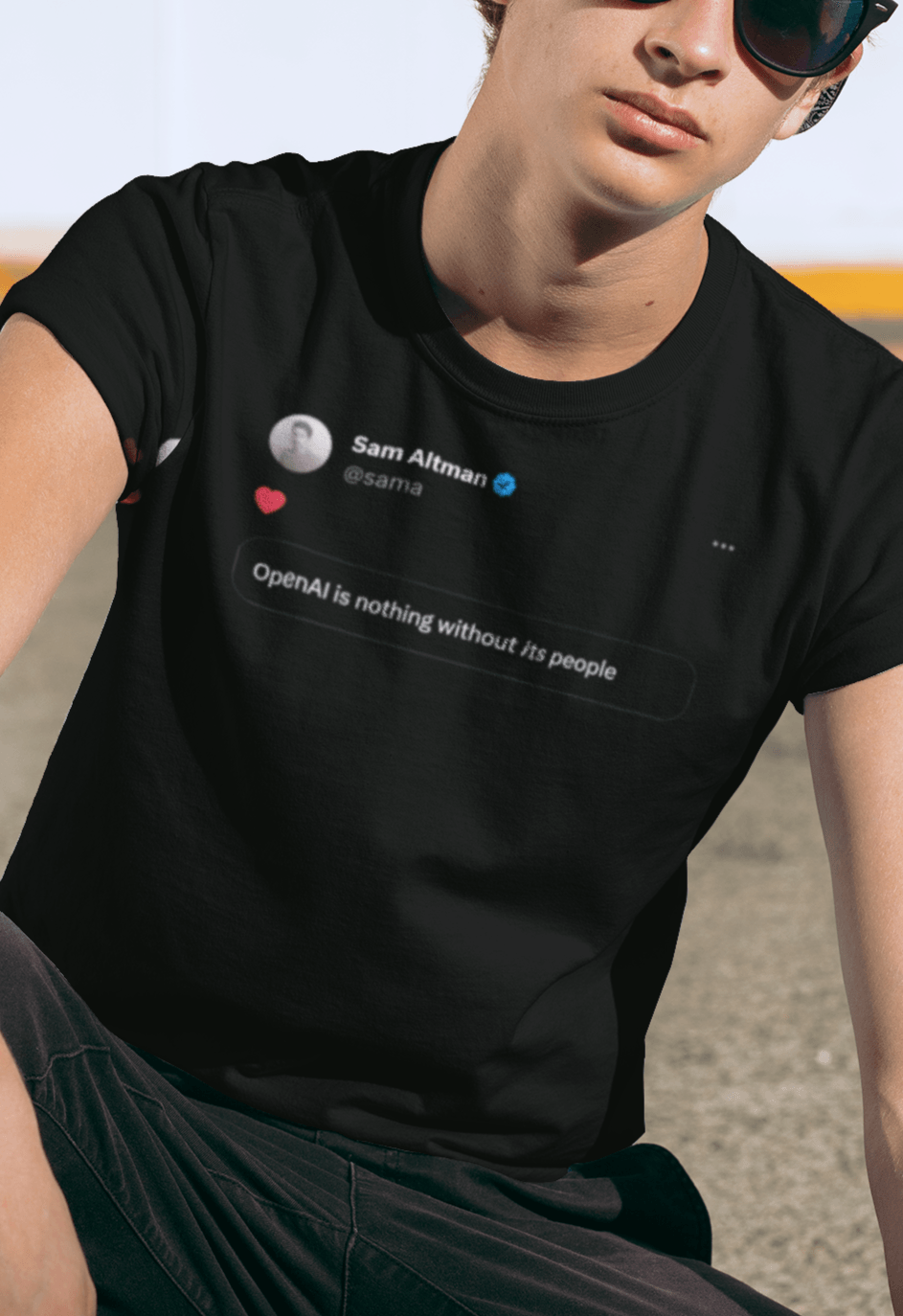 A person wears a black T-shirt featuring a tweet from Sam Altman that says &quot;OpenAI is nothing without its people&quot;.