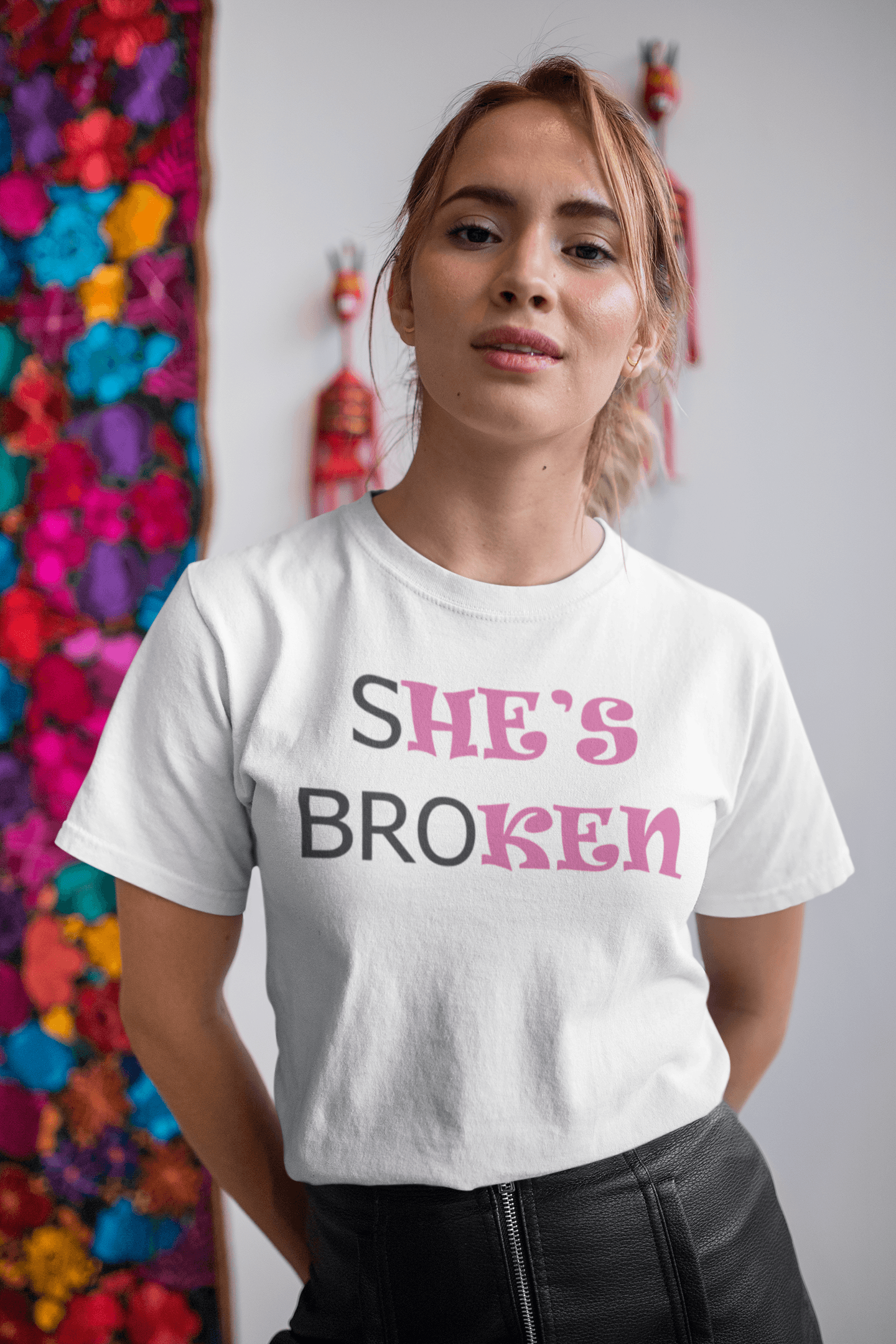 A woman in a white T-shirt that reads broth &quot;SHE&#39;S BROKEN&quot; and &quot;HE IS KEN&quot;, in pink and black text.