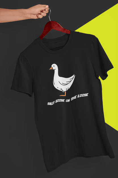 A black T-shirt with a cute mischievous goose in the middle, saying &quot;Silly goose on the loose&quot;, held by a hand against a split black and yellow background.