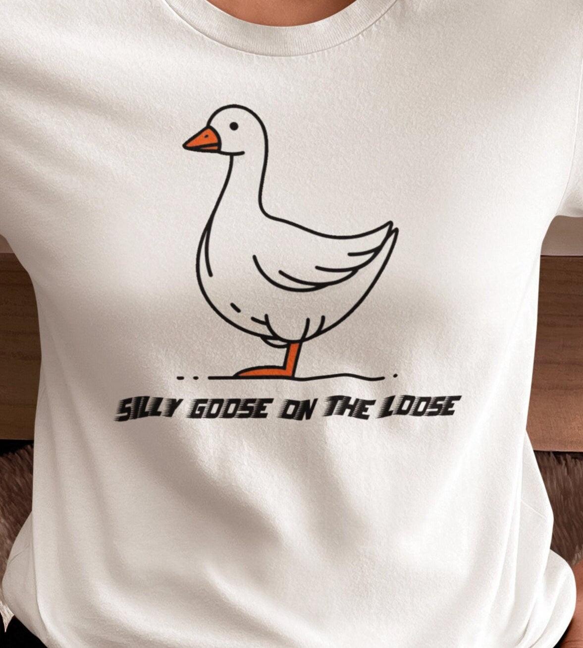 A woman wears a white T-shirt featuring a cute mischievous goose in the middle, saying &quot;Silly goose on the loose&quot;.