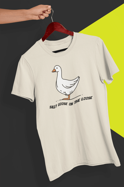 An off-white T-shirt with a cute mischievous goose in the middle, saying &quot;Silly goose on the loose&quot;, held by a hand against a split black and yellow background.