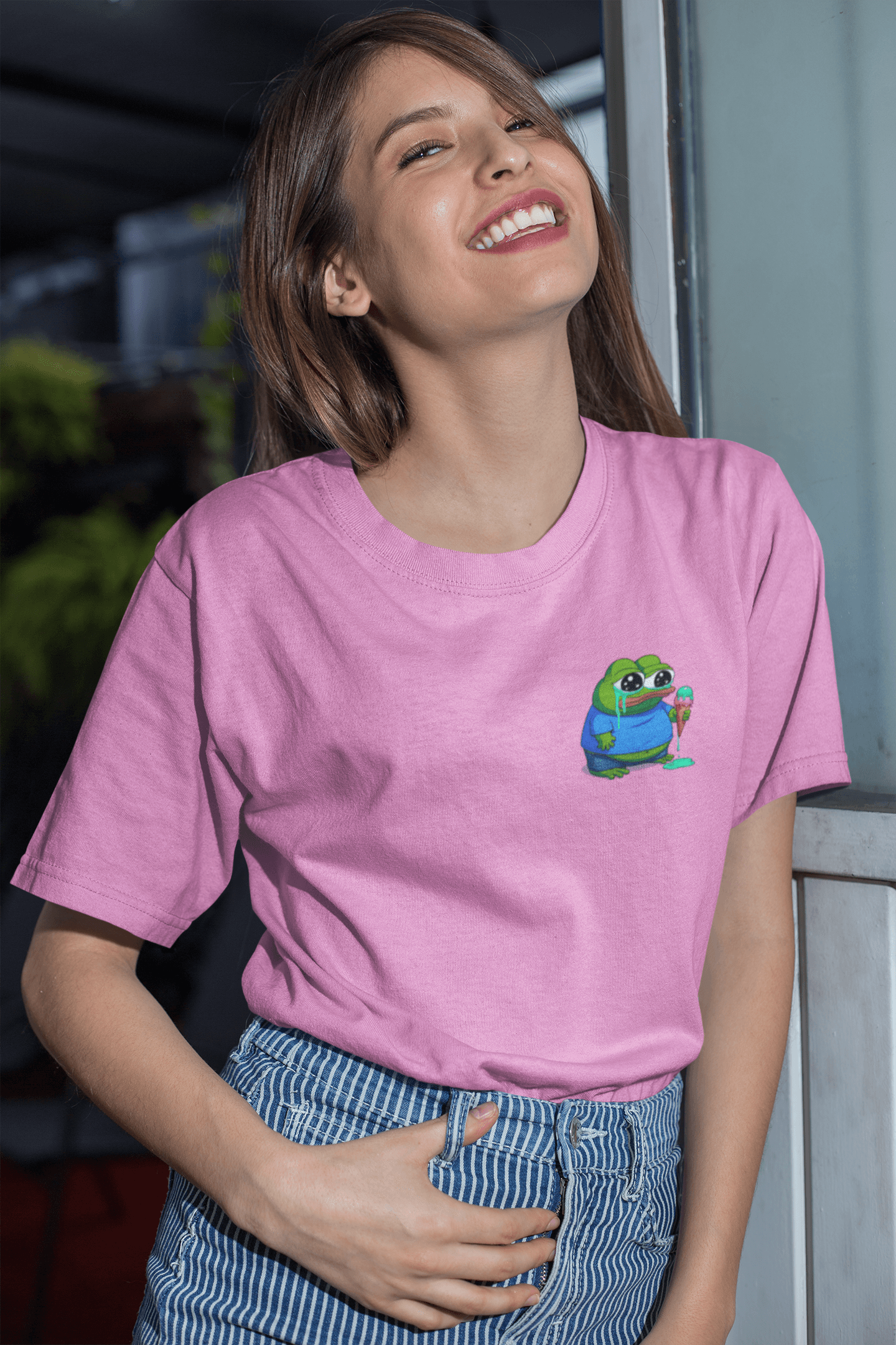 A woman wears a pink T-shirt featuring a small cute apu apustaja pepe in the right corner.